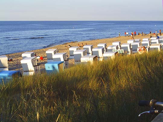Strand mit Strandkörben und Urlaubern bei untergehender Sonne